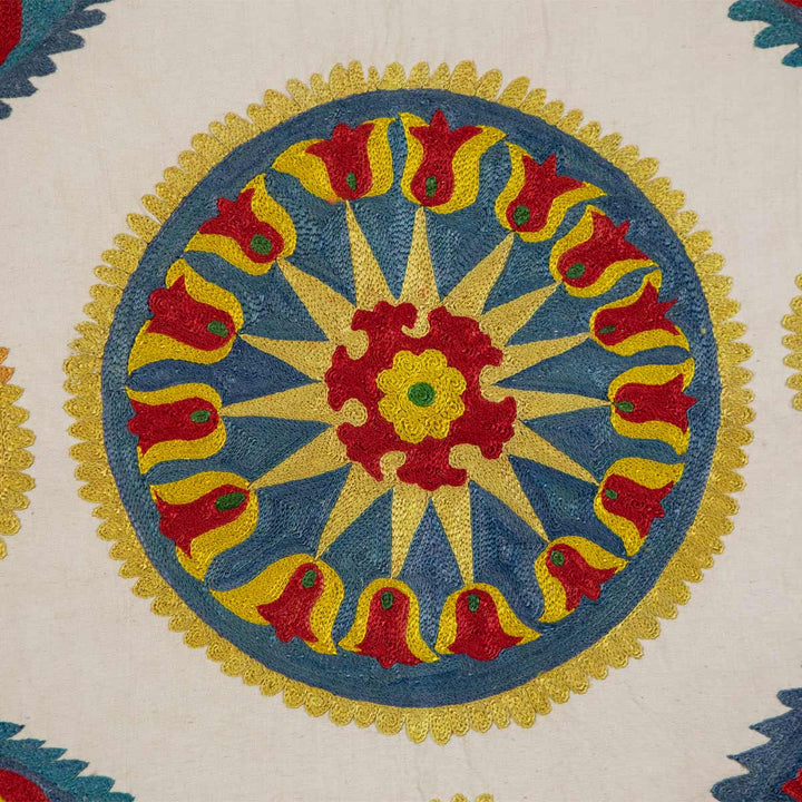 Detail view of Mekhann's cream iznik silk petite throw, showcasing the detailed embroidery around one of the medallion motifs if red, yellow, and blue silk threads, the cream silk canvas allows all the colours to stand out even more.