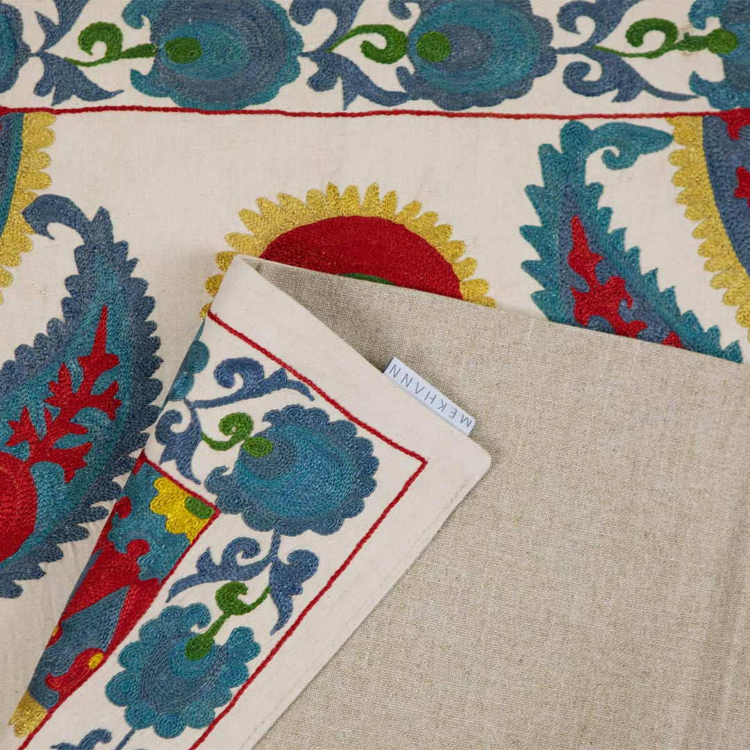 Folded view of Mekhann's cream iznik silk petite throw, slightly folded to reveal the fabric that lines the back of the throw.