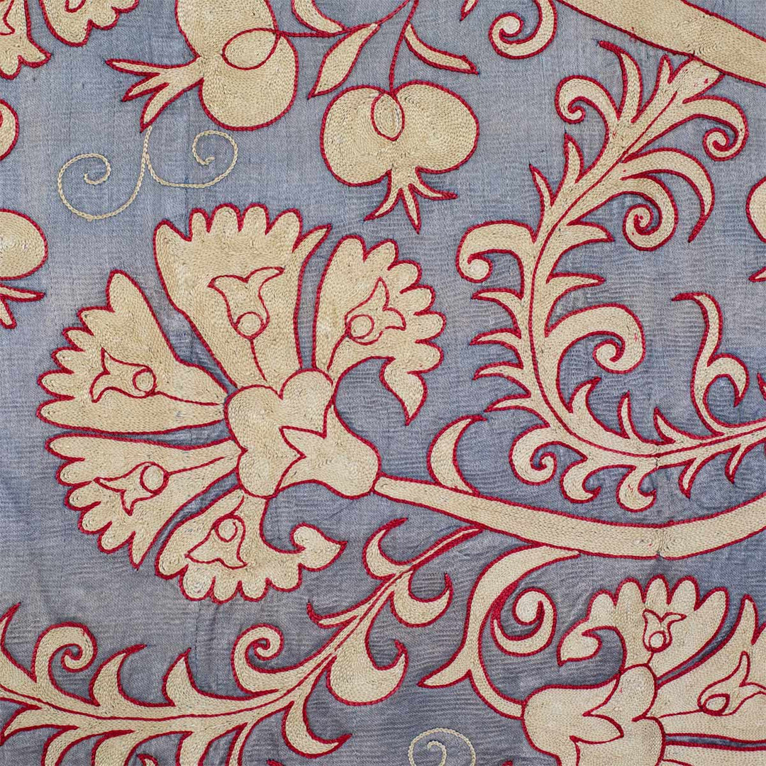 Close up view of Mekhann's pewter carnations throw, showing the details of the hand embroidered design motifs up close. We can see the cream carnations finished off the a red outlining to distinguish it from the pewter silk back.