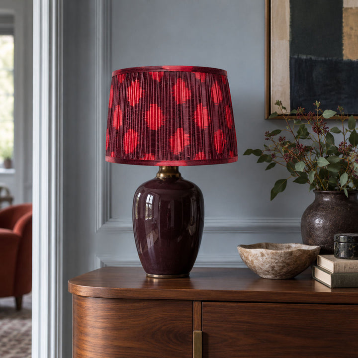 Maroon and fuchsia Polka Dot lampshade styled on an aubergine base beside a rust chair; illustrative living-room setting.