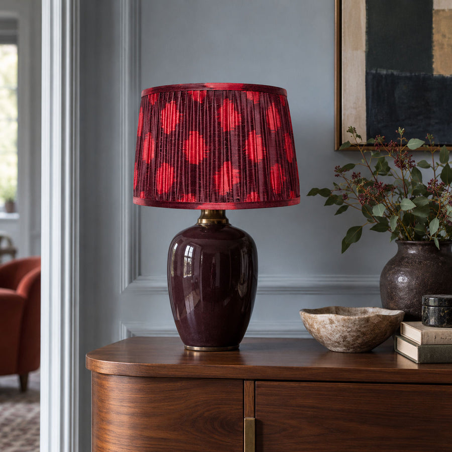 Maroon and fuchsia Polka Dot lampshade styled on an aubergine base beside a rust chair; illustrative living-room setting.