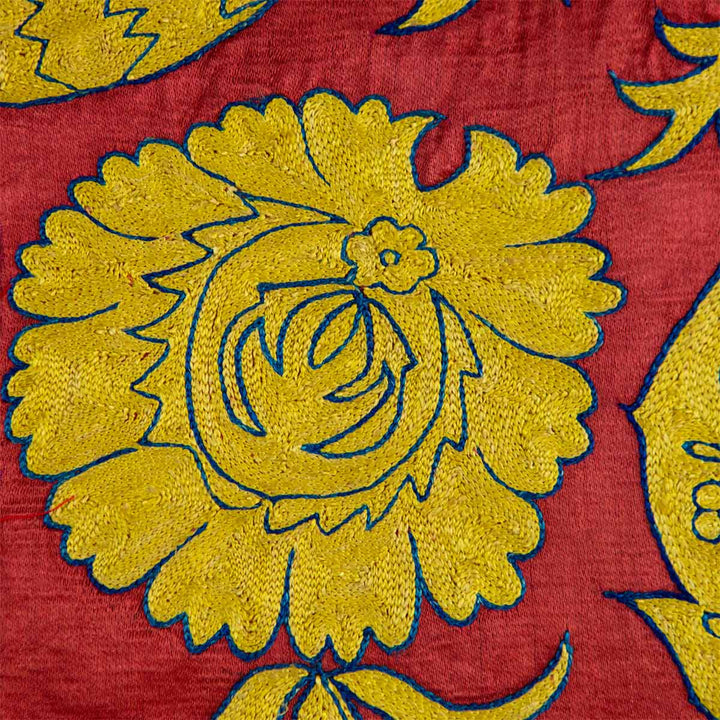Close up view of Mekhann's red botanical throw, showing one of the botanical motifs hand crafted with yellow silk, with a delicate blue outline to differentiate it front the bright red silk base.