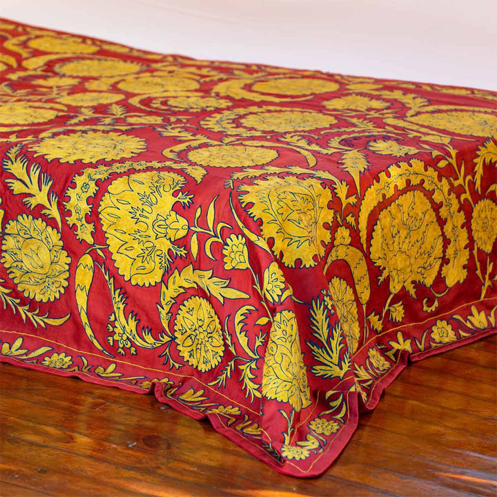 In use view of Mekhann's red botanical throw, where the throw has been draped at the foot of a bed display.