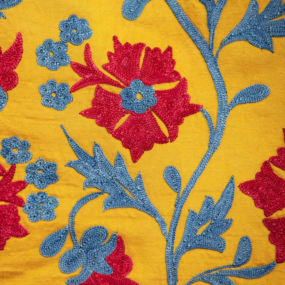 Close up view of Mekhann's embroidered botanical kaftan in saffron, showing the botanical focal motifs of the kaftan in vibrant red and bright blue.