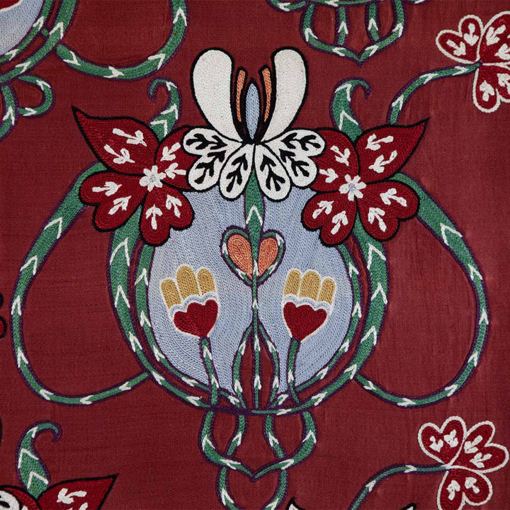Detailed view of Mekhann's maroon baroque petite throw, Up-close view of the maroon baroque throw showcasing the detailed embroidery work with white, red, and green floral accents on a silk maroon fabric.