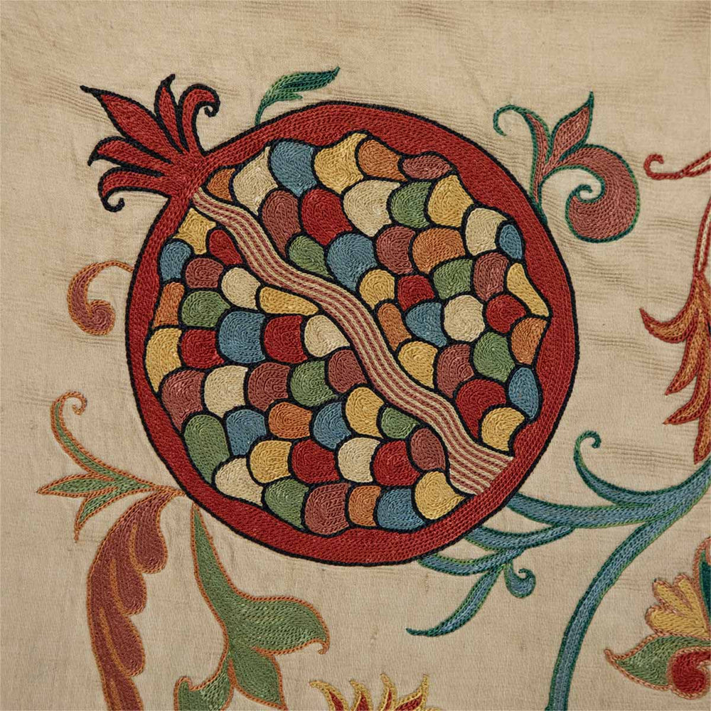 Close up view of Mekhann's cream iznik petite throw, displaying the fine attention to detail of embroidery and the vivid detail of the silk embroidered pomegranate design.