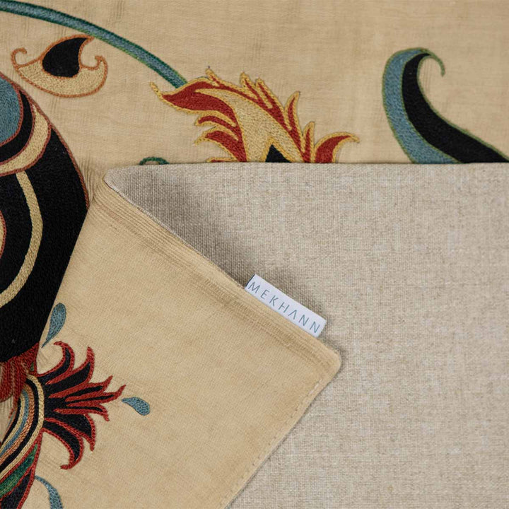 Folded view of Mekhann's cream iznik petite throw, highlighting the iznik patterns and fabric against the cream back lining with the Mekhann label.
