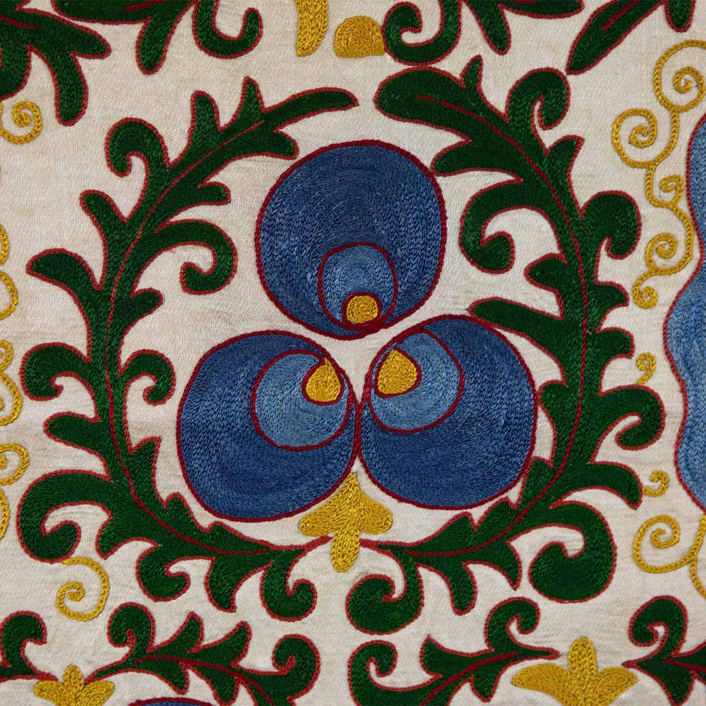Close up view of Mekhann's cream cintamani runner, displaying up close the hand embroidered cintamani motif in blue, surrounded by green leaf patterns. All of the hand embroidered elements set on a cream silk base.