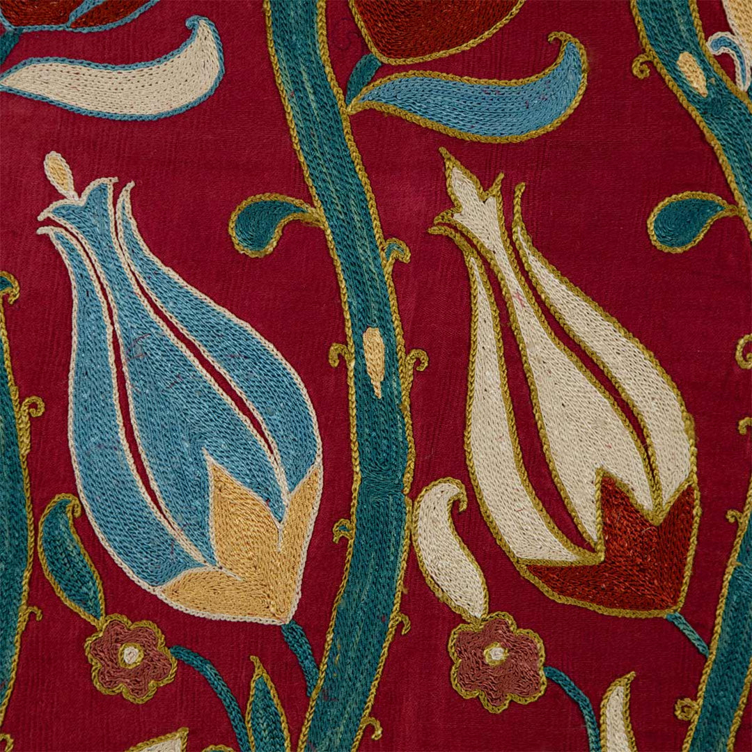 Detail view of Mekhann's maroon tulip petite throw, showing off the fine details of the stitch work done of two of the hand embroidered tulip motifs embroidered onto maroon coloured silk.
