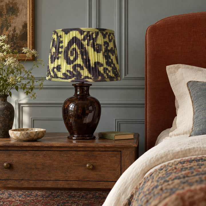 Volute lampshade styled on a dark ceramic base beside a terracotta headboard; illustrative bedroom setting.