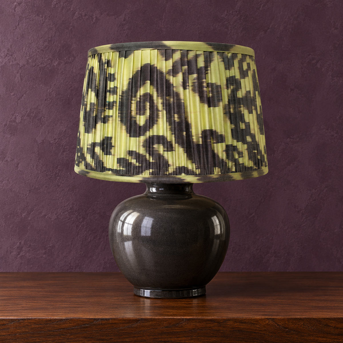 Volute lampshade styled on a dark ceramic base against muted aubergine plaster; illustrative full-lamp portrait.