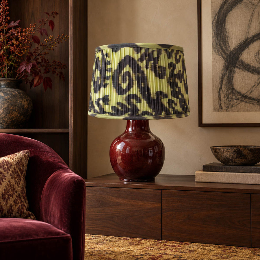 Volute lampshade styled on an oxblood ceramic base above a walnut console; illustrative sitting-room setting.
