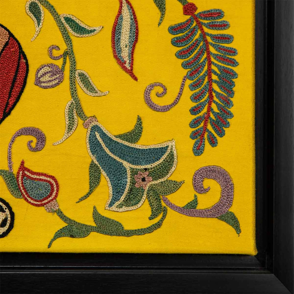 Corner view of Mekhann's yellow silk artwork with hand embroidered floral shapes, showing the corner of the black frame and where it joins to the yellow silk base.