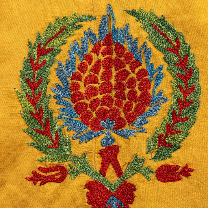 Close up view of Mekhann's embroidered arabesque kaftan in saffron, showcasing an arabesque motif in vibrant red, blue, and green silk yarns.