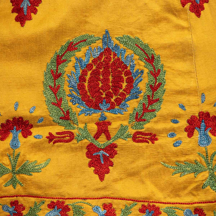 Detailed view of Mekhann's embroidered arabesque kaftan in saffron, with a display of bright red, blue and green patterns coming together to create a timeless design.
